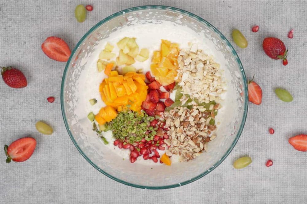 A bowl filled with cream topped with chopped fruits and nuts